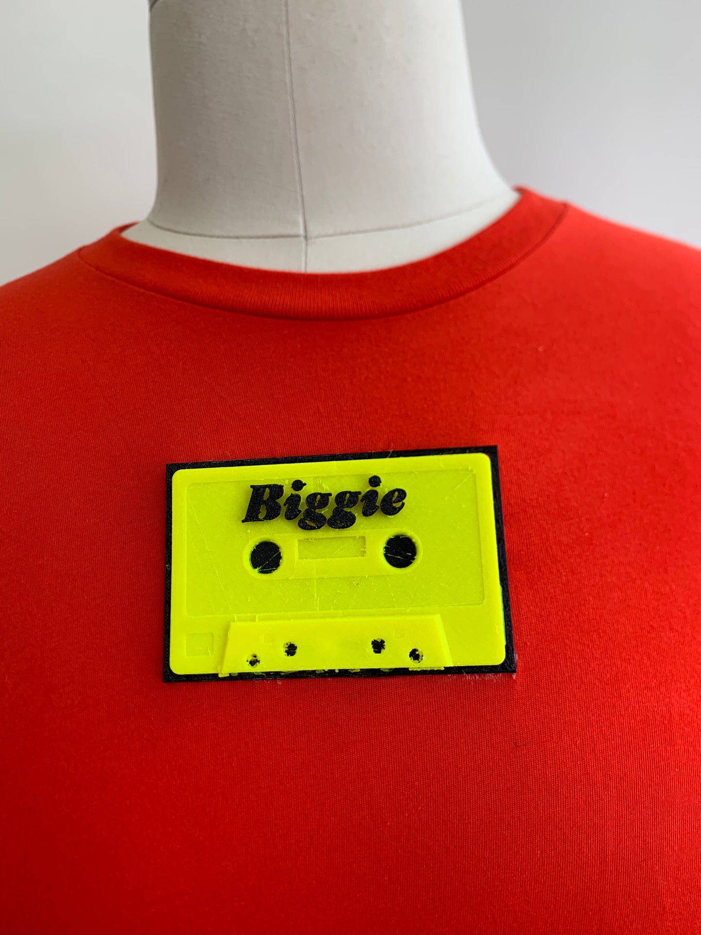 close up of red/orange shirt with a biggie  fluorescent yellow  cassette on chest