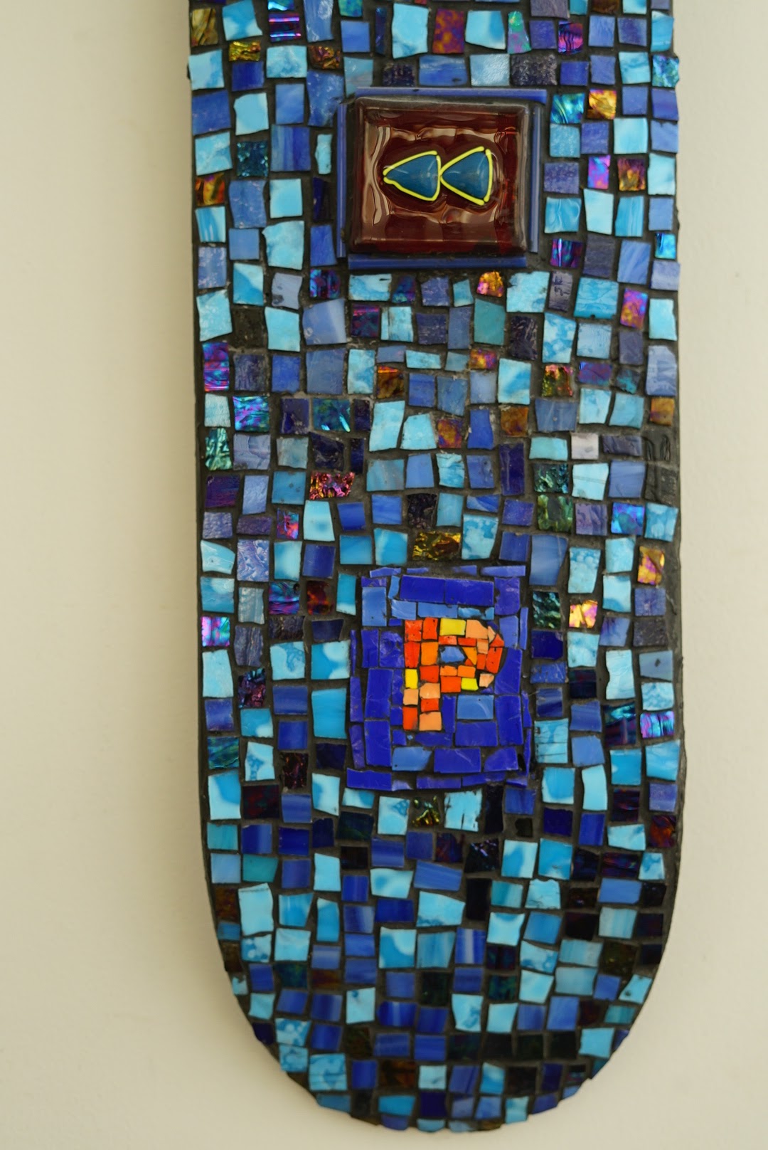 blue glass tile mosaic skateboard with the letter P in orange and the rewind sign