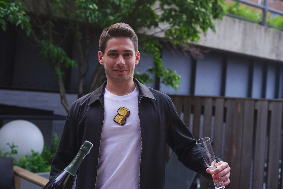 man wearing a mosaic champagne cork tee tshirt and holding a bottle of champagne and a flute