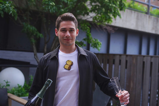 man wearing a mosaic champagne cork tee tshirt and holding a bottle of champagne and a flute