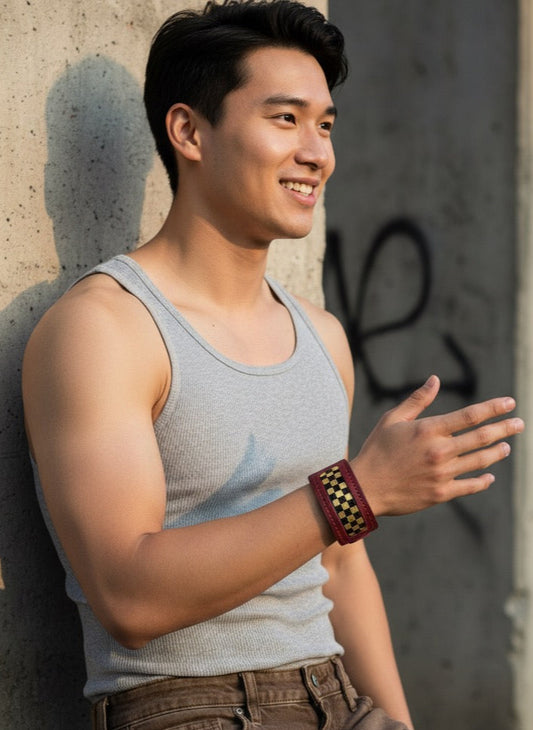 Man wearing a gray tank top and brown pants leaning against a wall.